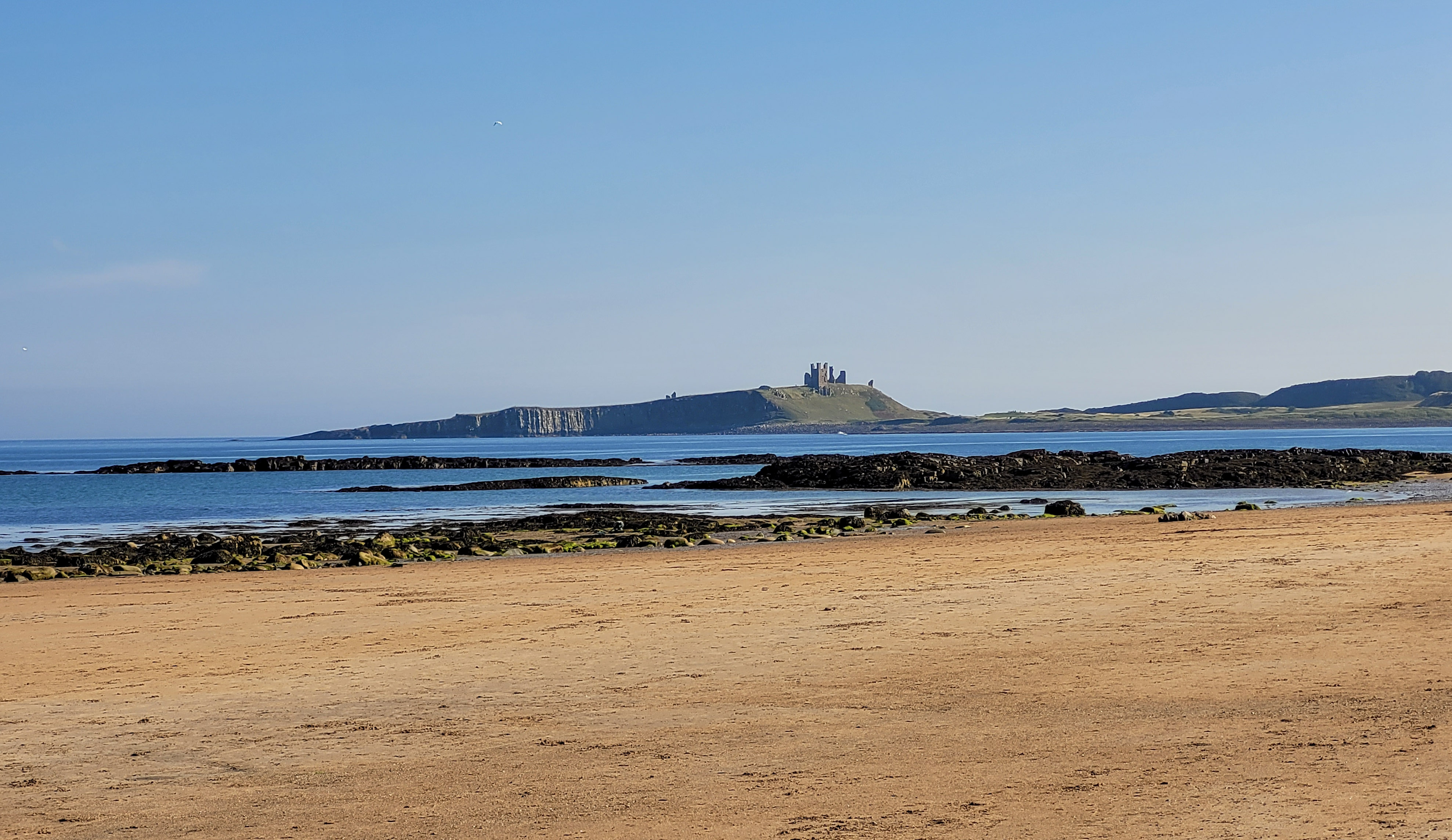 Photo of a beach and the sea, with a castle on a headland across the sea